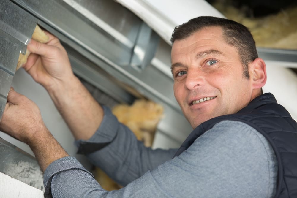 Tecnico sorridente installa pannelli metallici, mentre inserisce un isolante con una spatola in un cantiere.
